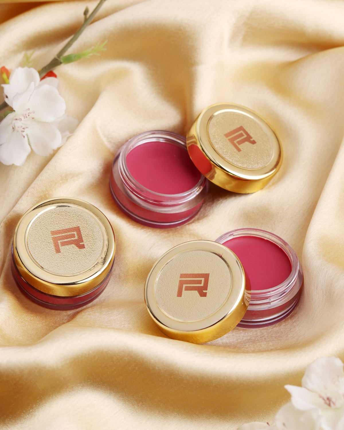 Gold-capped RAYZ tint pots on cream satin